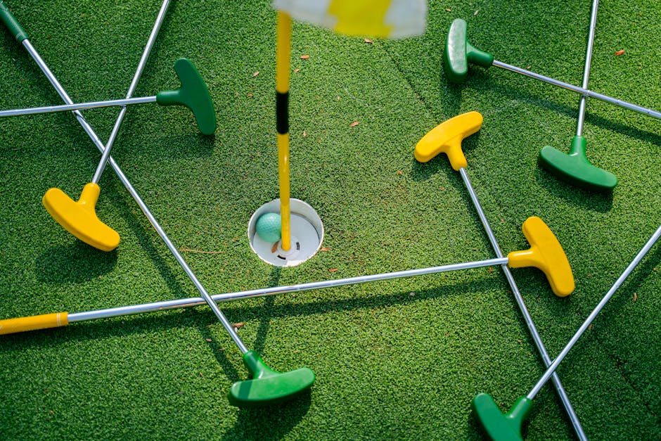 Top view of colorful mini golf putters around a hole on artificial grass.